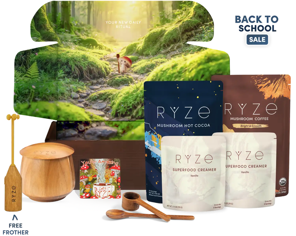 A RYZE wellness gift set arranged on a white background with a large forest-themed box behind it. Visible items include a wooden frother, a wooden container, a small magnet, two wooden spoons, two RYZE pouches (mushroom hot cocoa and mushroom coffee), and two creamer pouches, plus a 'Back to School Sale' badge and a 'Free Frother' offer graphic.