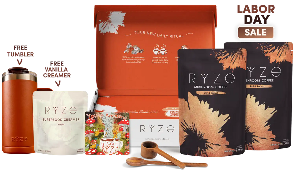 A RYZE gift set displayed on a white background with a 'LABOR DAY SALE' badge in the top right. The set includes a rust-colored insulated tumbler, a pouch of RYZE Superfood Creamer, a box of RYZE Mushroom Coffee, a box of RYZE Vanilla Creamer, a colorful RYZE magnet, a wooden scoop, and a wooden spoon, with the open orange gift box in the center.